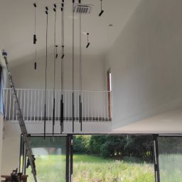 Regimex licencjonowany wykonawca firmy RIGIPS Polska. - Wnętrze w trakcie wykańczania z wysokim sufitem i zainstalowanym oświetleniem punktowym, widoczna drabina i elementy zabudowy kuchennej.