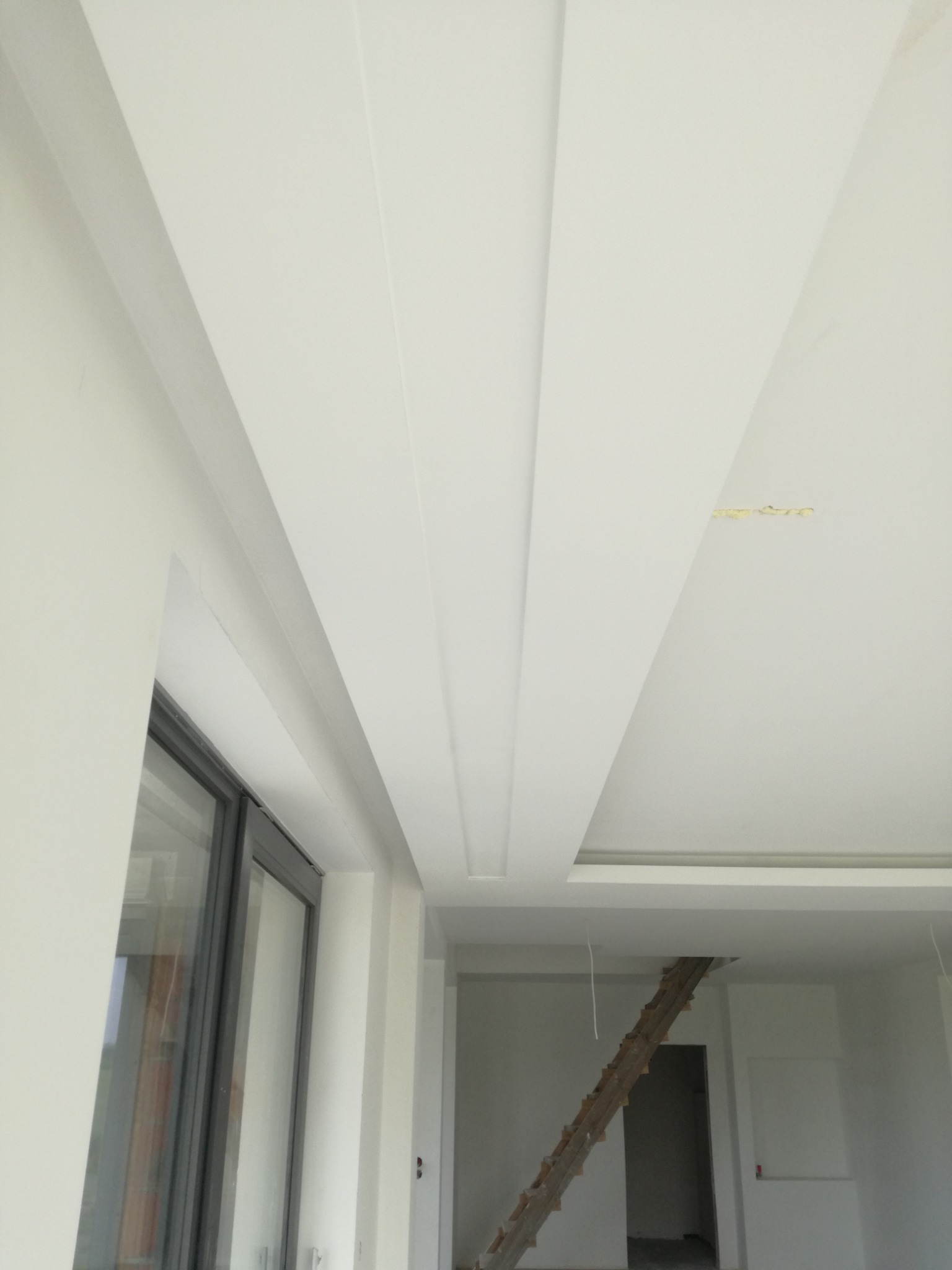 Biały sufit z dekoracyjnymi, podłużnymi wgłębieniami i oświetleniem w nowym wnętrzu, widok z dołu, drabina w tle.