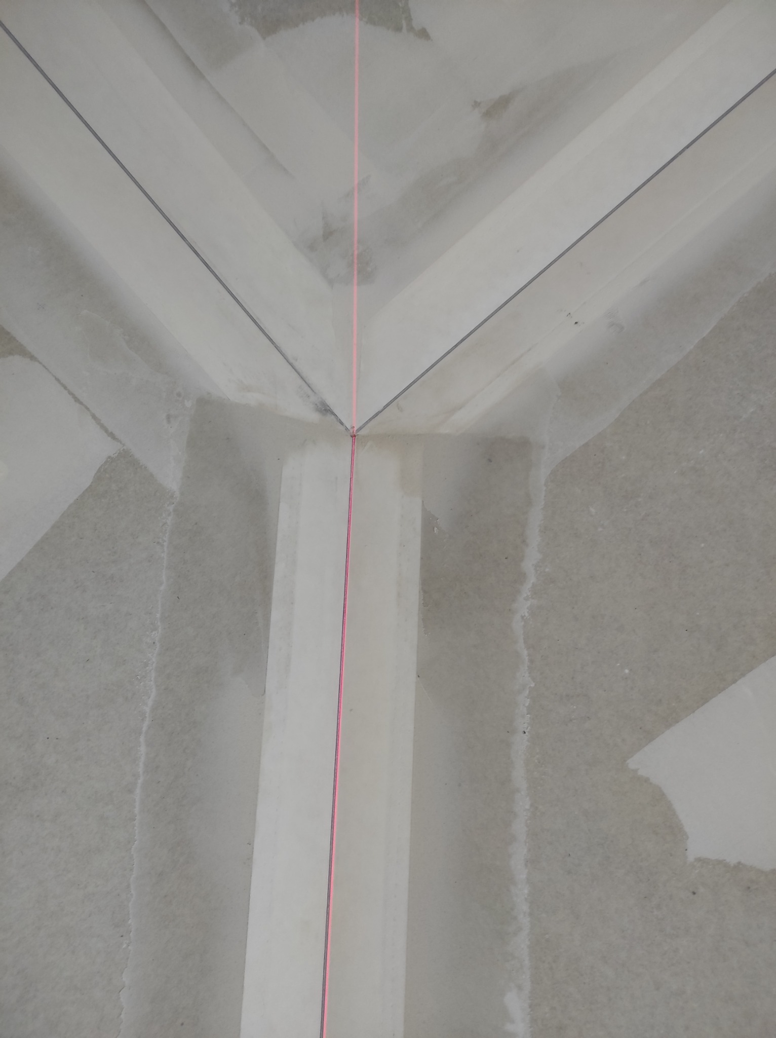 Kąt sufitu i ściany w trakcie prac wykończeniowych, widoczna laserowa linia wyznaczająca poziom, ślady szpachli i łączenia płyt.