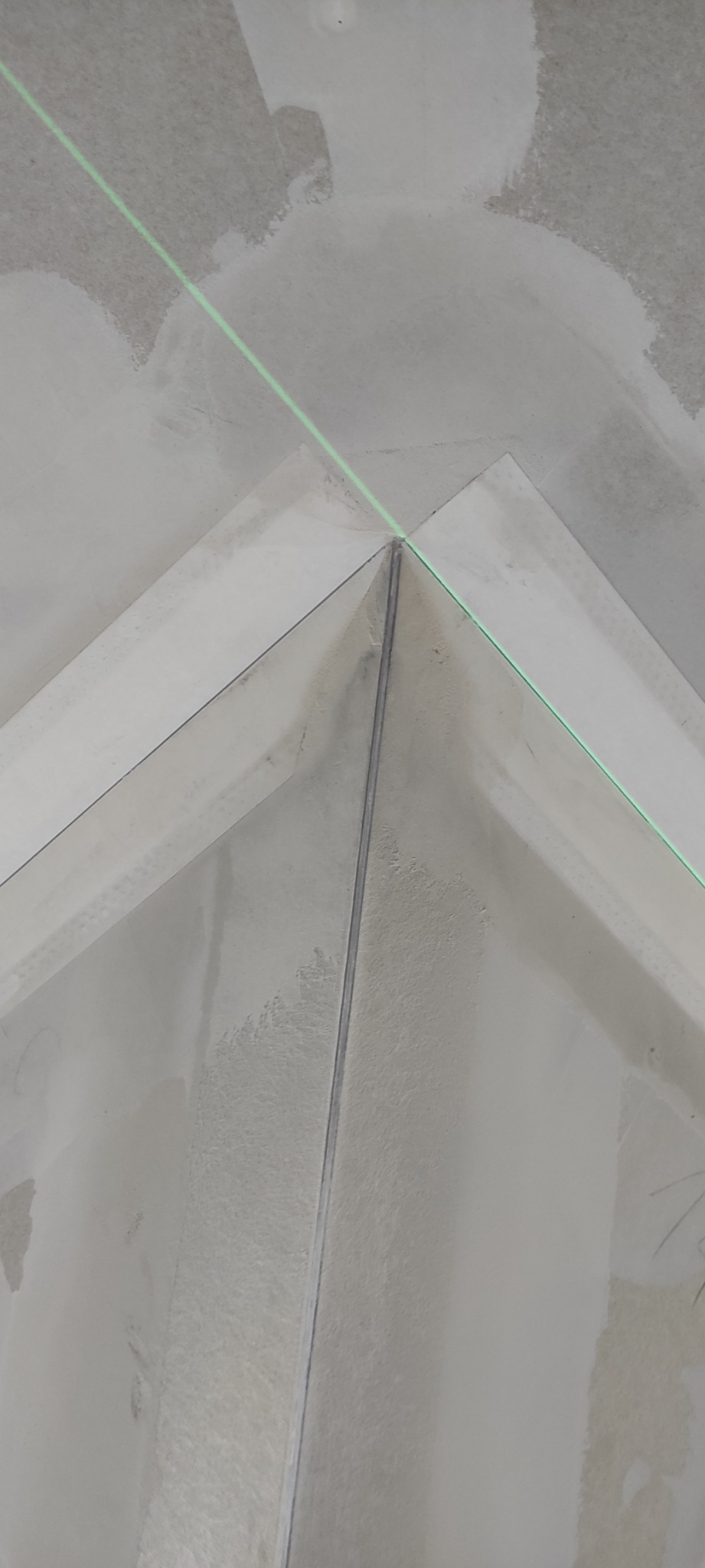 Kąt wewnętrzny sufitu z zamontowaną płytą, widoczna linia lasera wyznaczająca poziom, ślady szpachlowania na powierzchni.