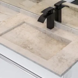 Beżowy blat łazienkowy z kamienia z wpuszczoną umywalką i nowoczesną, czarną armaturą, odbijający się w lustrze.