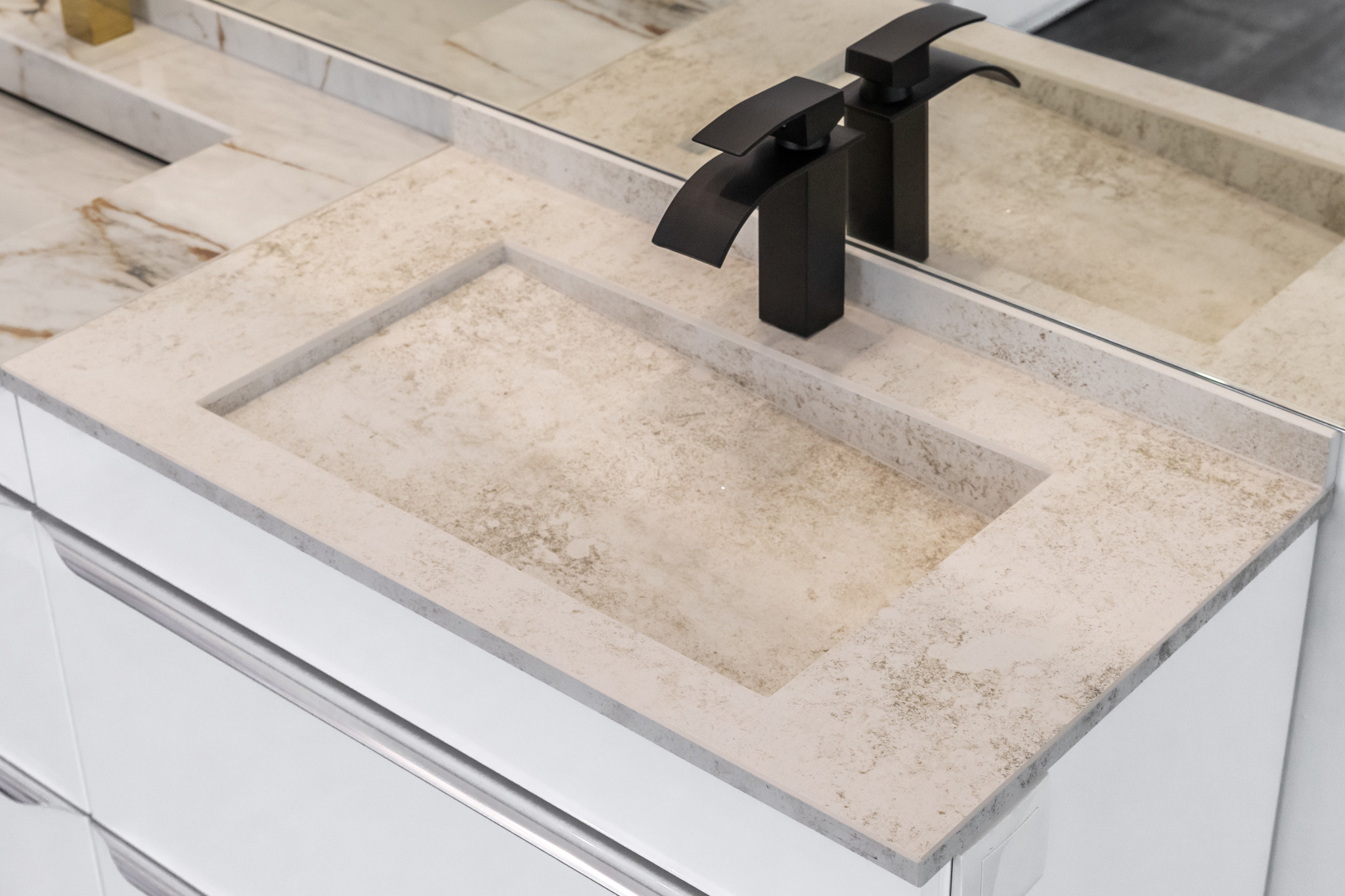 Beżowy blat łazienkowy z kamienia z wpuszczoną umywalką i nowoczesną, czarną armaturą, odbijający się w lustrze.