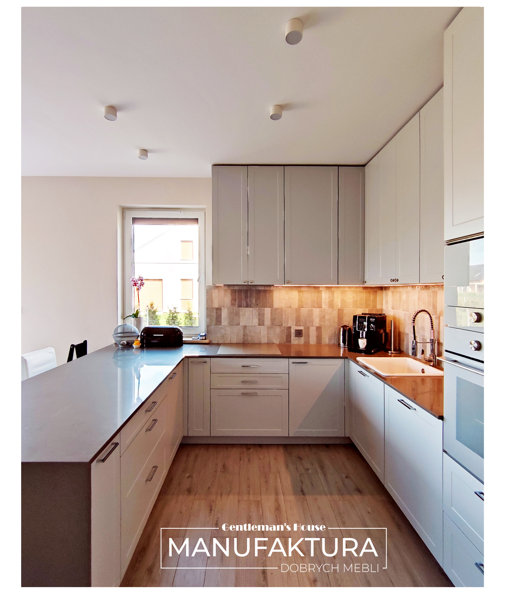 Nowoczesna kuchnia w odcieniach bieli i szarości, z drewnianą podłogą i blatem oraz oświetleniem podszafkowym, ekspres do kawy na blacie.