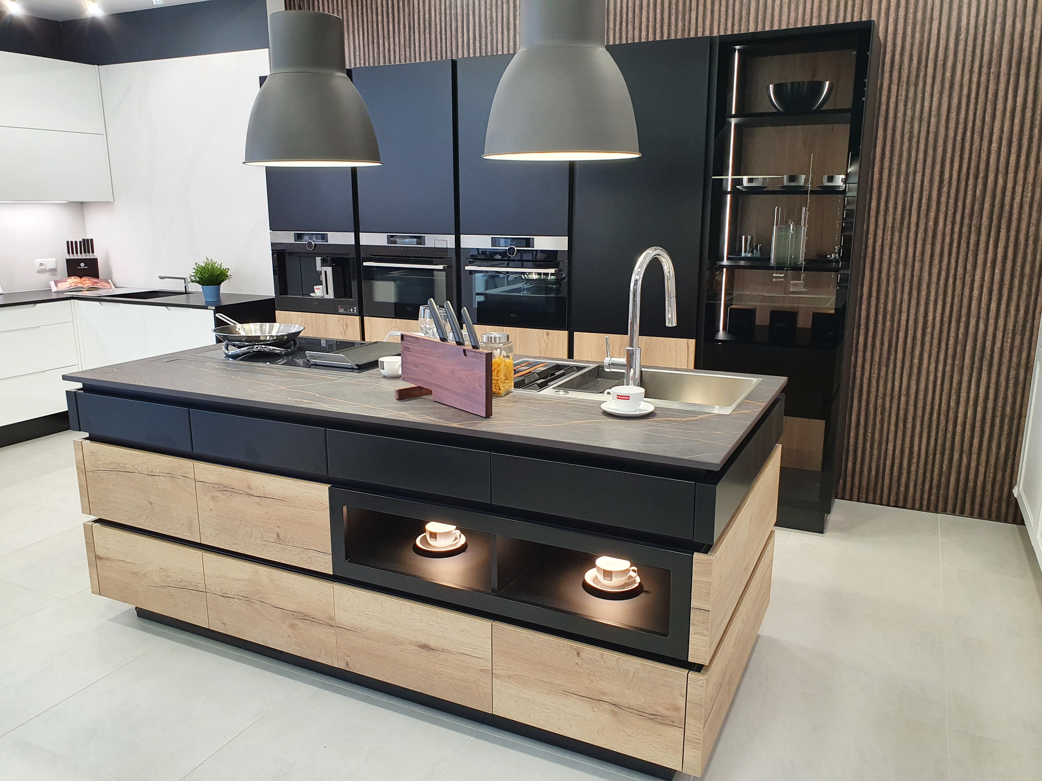 Nowoczesna wyspa kuchenna z blatem w odcieniach szarości, oświetlona lampami wiszącymi, z ekspozycją filiżanek w dolnej części, zrealizowana w Świdnicy.