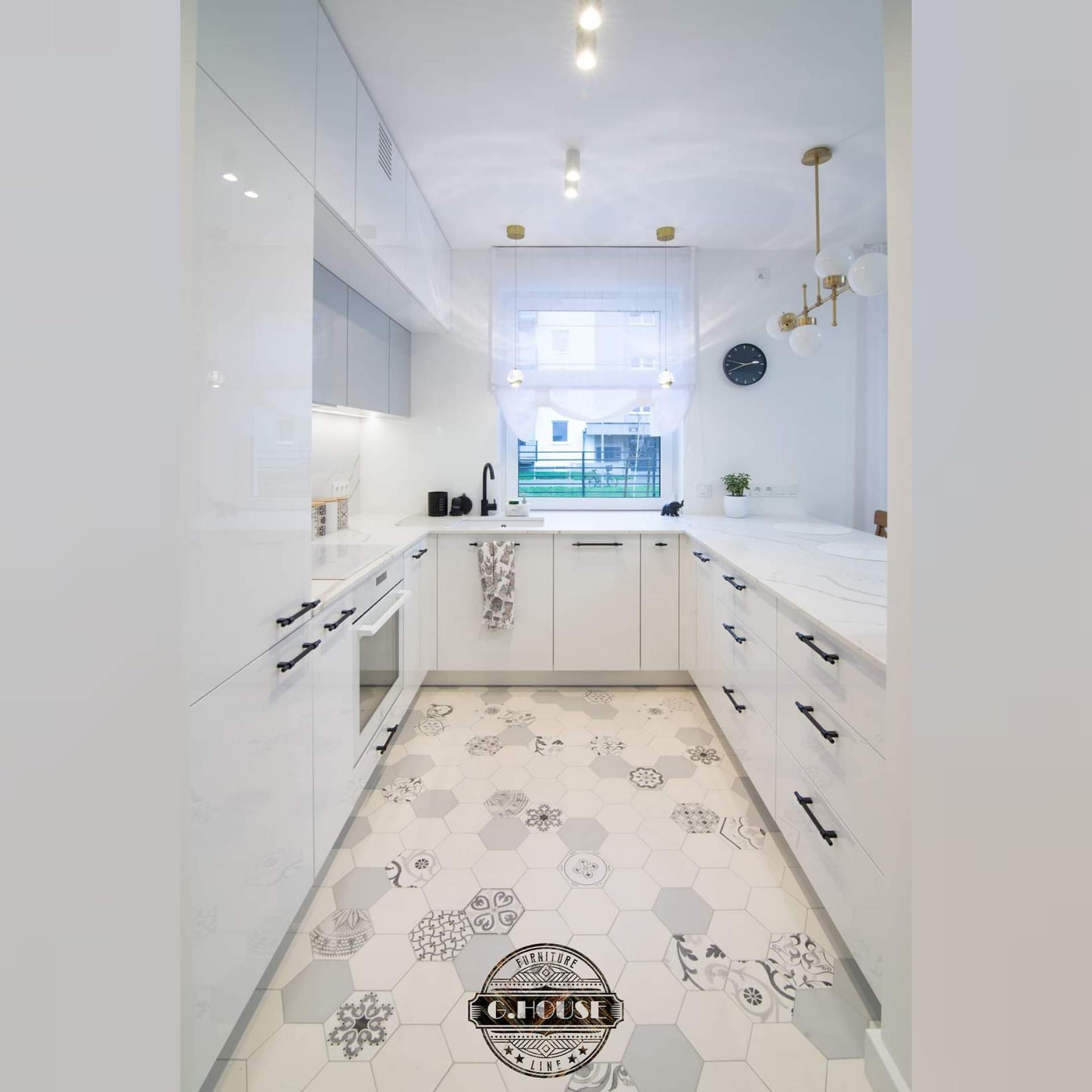 Jasna, nowoczesna kuchnia z białymi szafkami, blatem imitującym marmur i heksagonalną podłogą z wzorami, oświetlona wiszącymi lampami.