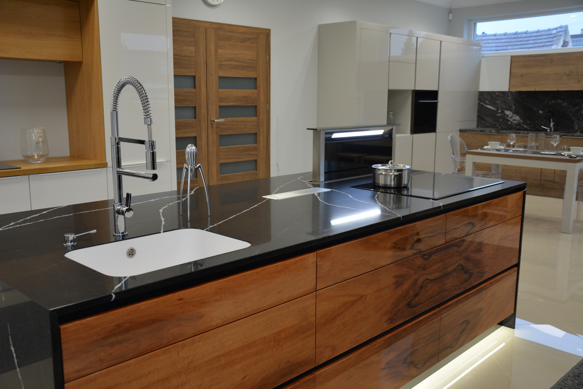 Nowoczesna kuchnia z wyspą o czarnym blacie z białym żyłkowaniem i drewnianymi frontami szuflad, chromowana bateria i akcesoria, płyta indukcyjna i wysuwany okap.
