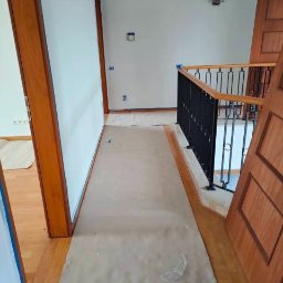 LT Łukasz Tabor - Korytarz w trakcie zabezpieczania folią malarską przed pracami wykończeniowymi, widoczne przygotowane ściany i drewniane elementy.