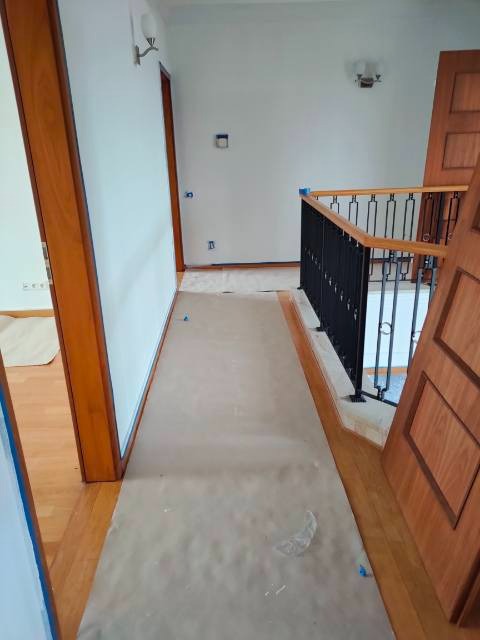 Korytarz w trakcie zabezpieczania folią malarską przed pracami wykończeniowymi, widoczne przygotowane ściany i drewniane elementy.