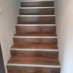 Schody wykończone panelami imitującymi drewno z jasnymi listwami zabezpieczającymi krawędzie stopni, widok z dołu.