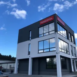 Dwukondygnacyjny budynek biurowy w nowoczesnej kolorystyce: białe i grafitowe ściany, duże okna z odbiciem nieba, czerwone logo na dachu.