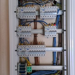 FAME INSTAL - Otwarta skrzynka elektryczna z zainstalowanymi bezpiecznikami, przewodami w różnych kolorach i listwami zaciskowymi, widoczne elementy montażowe i oznaczenia na urządzeniach.