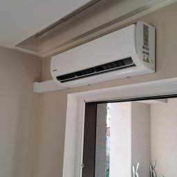 FAME INSTAL - Biały klimatyzator Kaisai zamontowany na ścianie nad drzwiami balkonowymi, z widocznym wyświetlaczem wskazującym temperaturę 17 stopni Celsjusza, w tle widok na balkon z narzędziami ogrodniczymi.