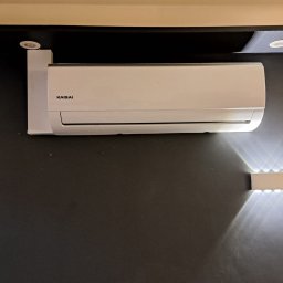 FAME INSTAL - Biały klimatyzator Kaisai zamontowany na ciemnoszarej ścianie, widoczne oświetlenie sufitowe i listwa LED.