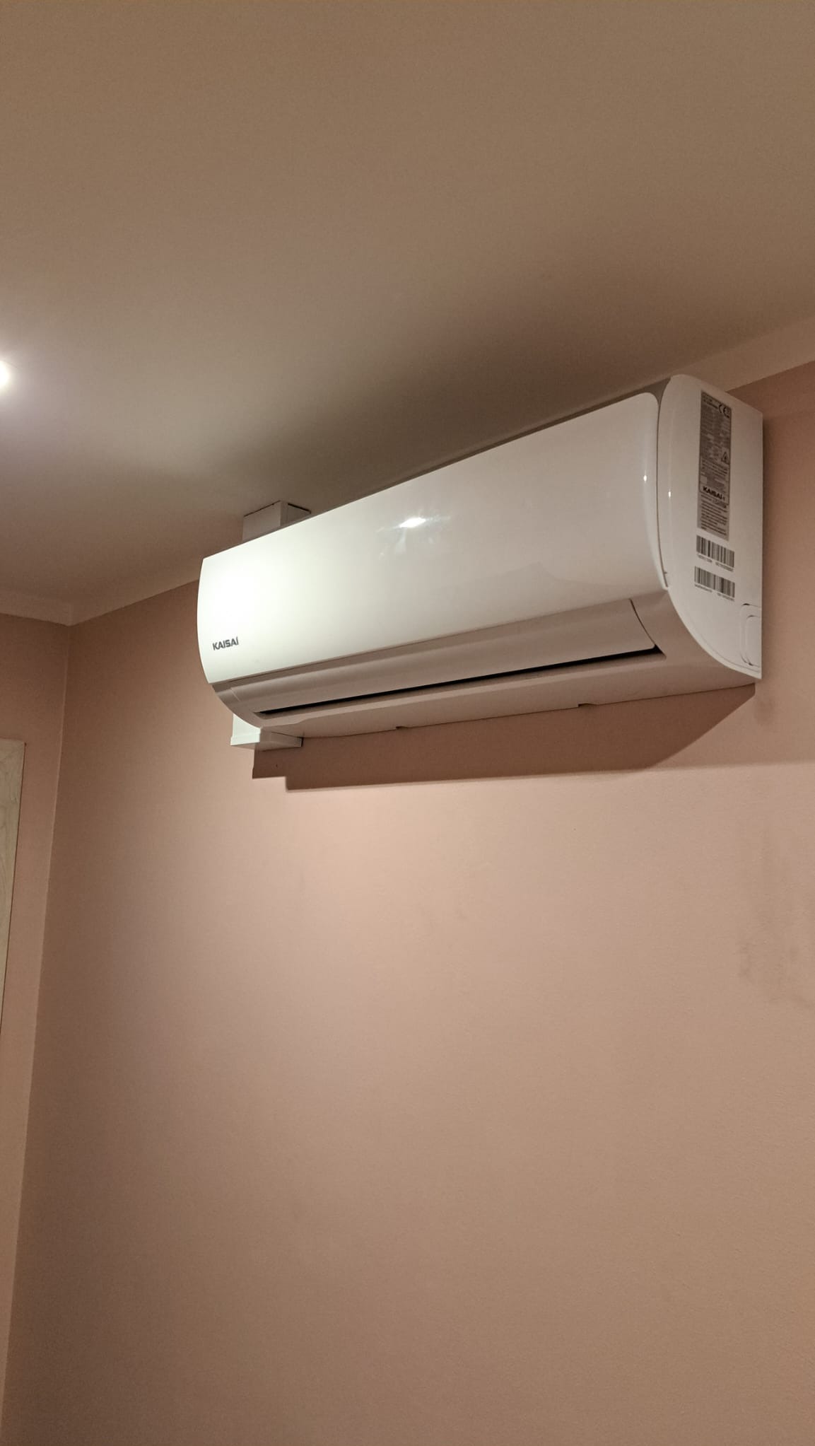 Biały klimatyzator Kaisai zamontowany na różowej ścianie, widoczne detale obudowy i etykiety informacyjne.