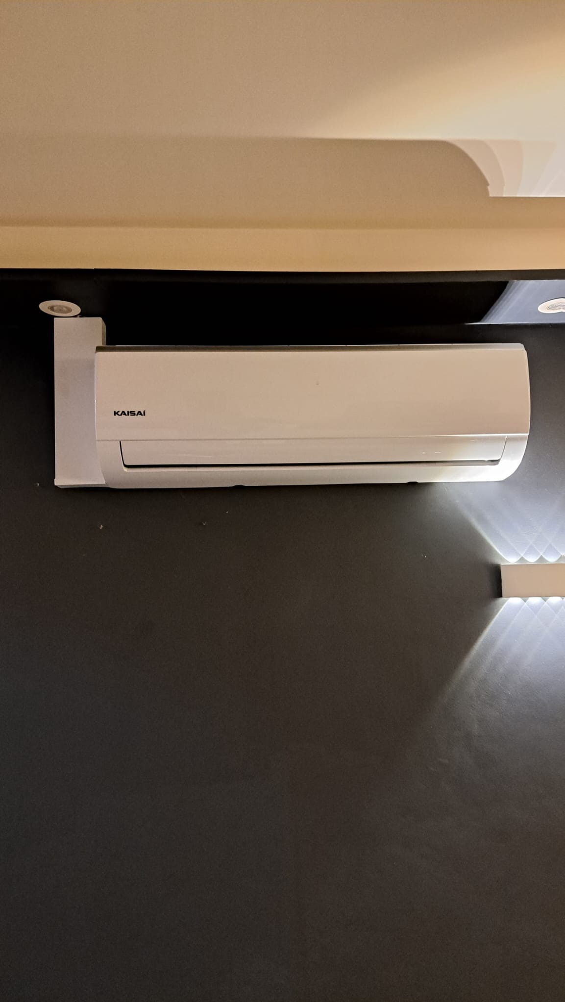Biały klimatyzator Kaisai zamontowany na ciemnoszarej ścianie, widoczne oświetlenie sufitowe i listwa LED.