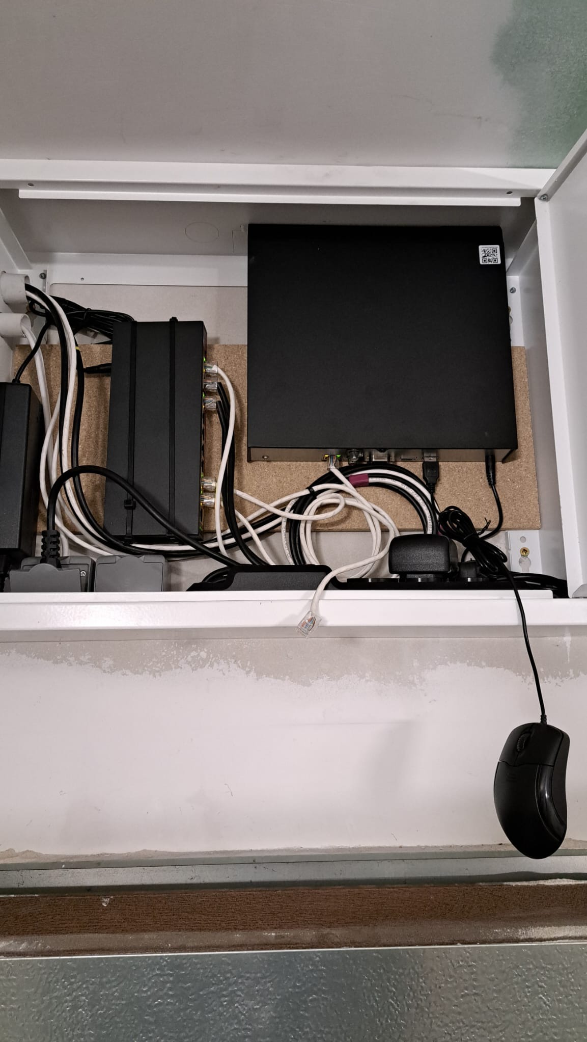 Rozdzielnica elektryczna z przewodami i urządzeniami, widok z dołu, kabel sieciowy z wtyczką RJ45 zwisa luźno, obok leży myszka komputerowa.