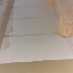 Ułożone betonowe płyty chodnikowe z dekoracyjnym żwirem w przestrzeniach między nimi, obok drewniany stół z ławkami o surowym wykończeniu.