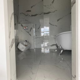 MAPRO SP.Z.O.O - Nowoczesna łazienka w trakcie remontu z białą wanną na lwich nóżkach, marmurowe płytki na ścianach i podłodze, oraz zabezpieczona folią toaleta w rogu.