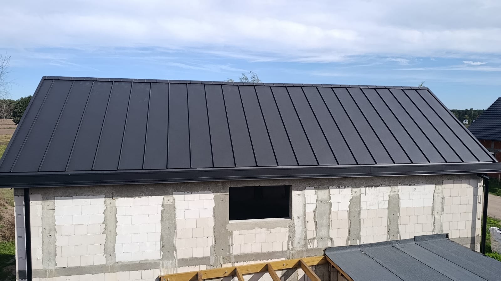 Czarny dach z blachy na budynku w trakcie budowy, widok z góry, Dąbcze. Nowoczesne pokrycie dachowe z orynnowaniem. Elementy konstrukcji dachu widoczne w dolnej części kadru.