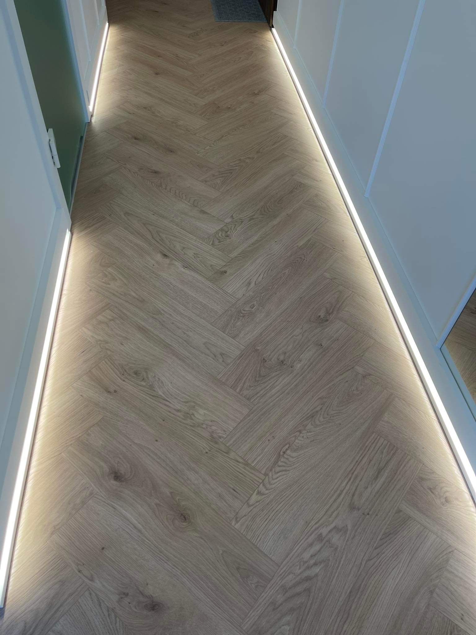 Parkiet ułożony w jodełkę z oświetleniem LED wzdłuż ściany i szafy wnękowej.