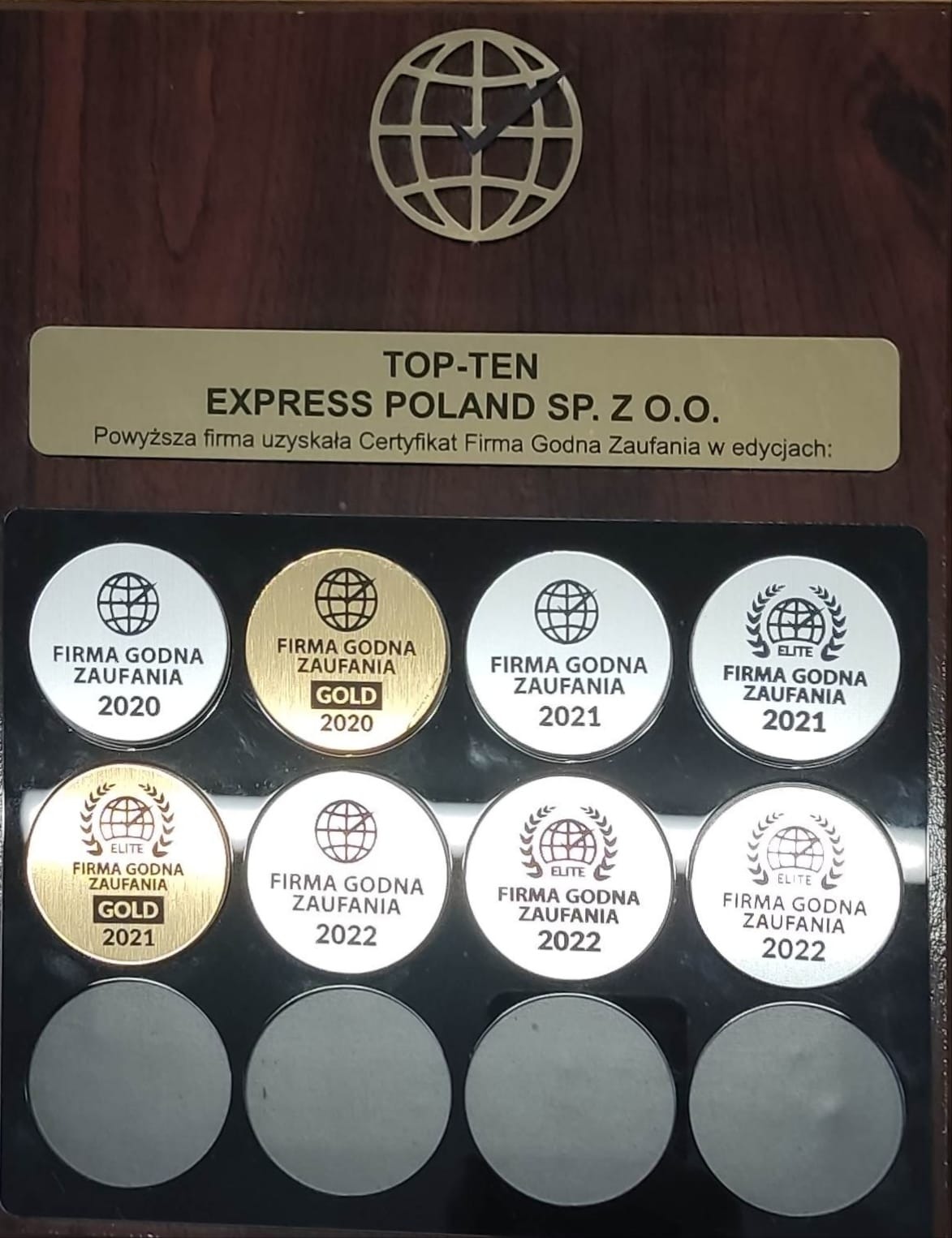 Tablica z certyfikatami 'Firma Godna Zaufania' dla Express Poland Sp. z o.o. z lat 2020-2022, niektóre w wersji Gold i Elite, umieszczona na drewnianym tle z dekoracyjnym globusem u góry.