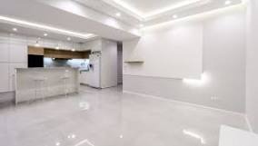 Białe, minimalistyczne wnętrze: kuchnia otwarta na salon, jasna podłoga z połyskiem, oświetlenie sufitowe LED tworzące nowoczesny efekt.