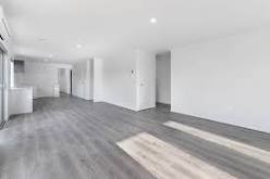 Puste, nowocześnie wykończone wnętrze mieszkania z szarymi panelami podłogowymi, białymi ścianami i widocznym klimatyzatorem na ścianie, przygotowane do odbioru.