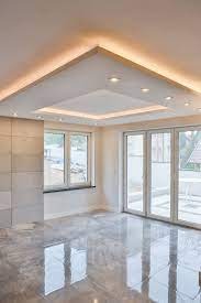 Pusty, jasny pokój z marmurową podłogą, dużymi oknami i nowoczesnym sufitem podwieszanym z oświetleniem LED w kształcie trójkąta i kwadratu.