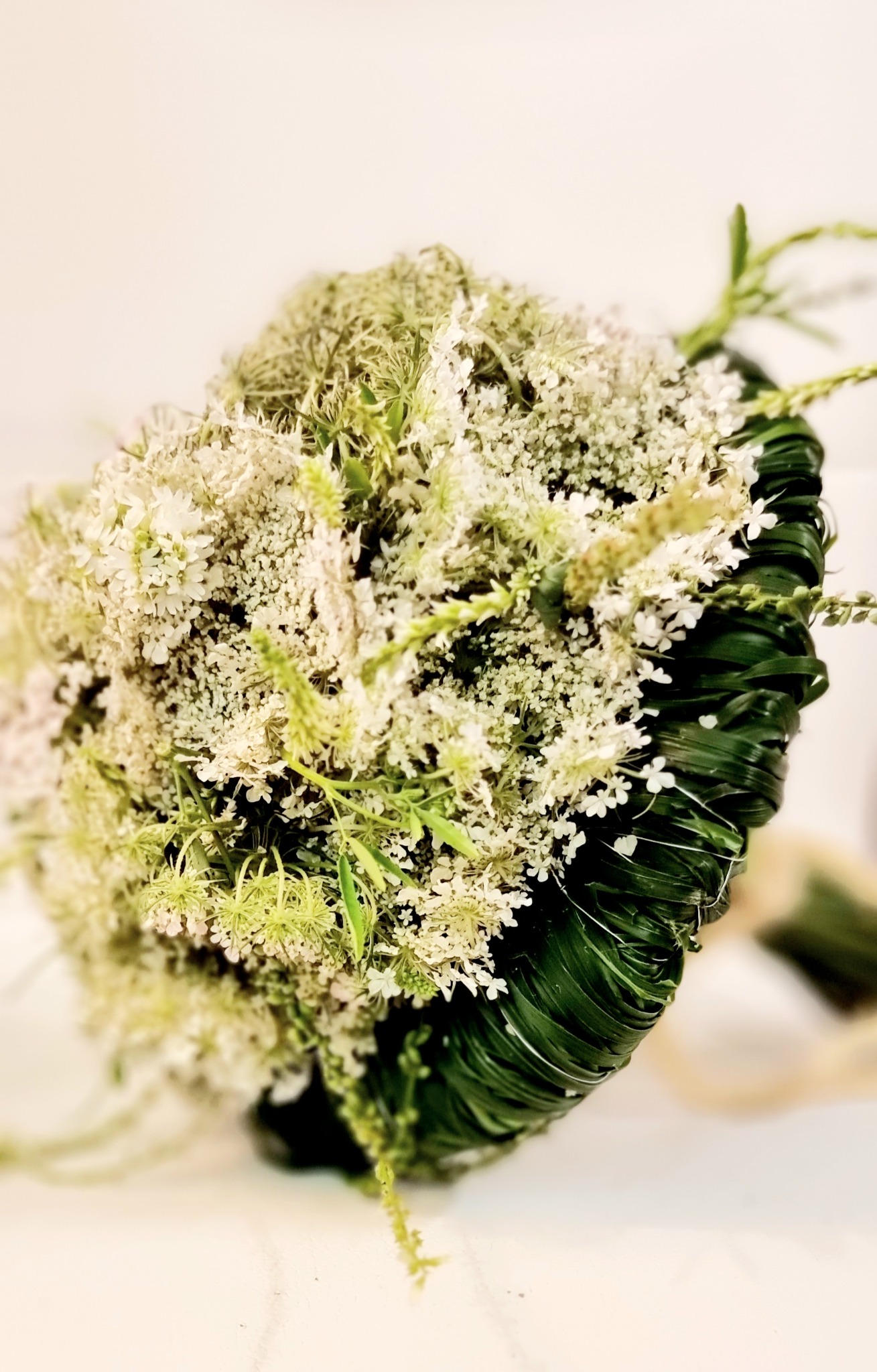 Delikatny bukiet z białych kwiatów i zielonych liści, starannie ułożony i związany, prezentowany przez kwiaciarnię w Szczecinie.