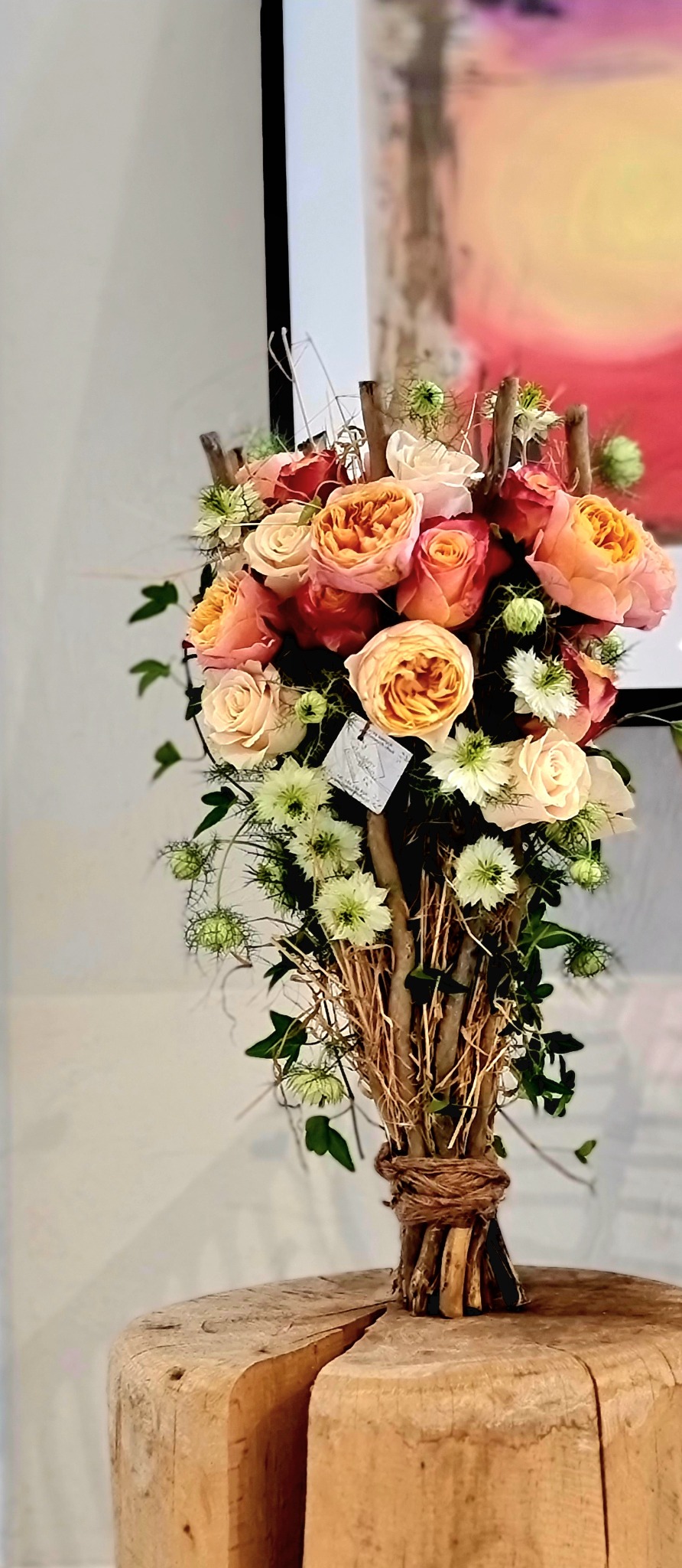 Rustykalny bukiet z róż w odcieniach brzoskwini i bieli, związany sznurkiem i gałązkami, z małą karteczką, na tle rozmytego obrazu.