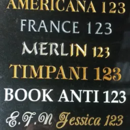 Czarna kamienna tablica z wygrawerowanymi nazwami różnych krojów pisma i numerem 123, w odcieniach złota, srebra i bieli, prezentująca liternictwo w kamieniu.
