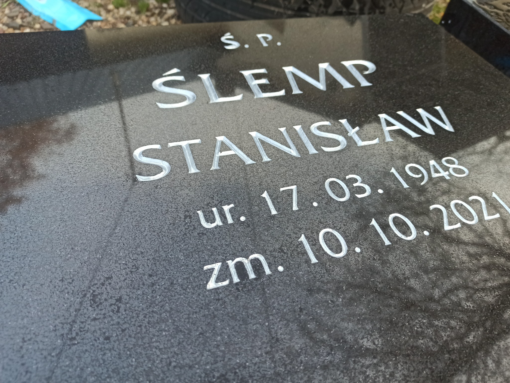 Ciemny, granitowy nagrobek z wygrawerowanym imieniem i nazwiskiem Ś.P. ŚLĘMP STANISŁAW, datą urodzenia 17.03.1948 i datą śmierci 10.10.2021.
