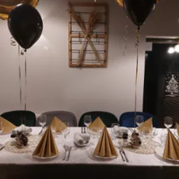 Elegancko nakryty stół z złotymi serwetkami, czarnymi balonami i dekoracją w kształcie choinki, przygotowany na uroczystość.