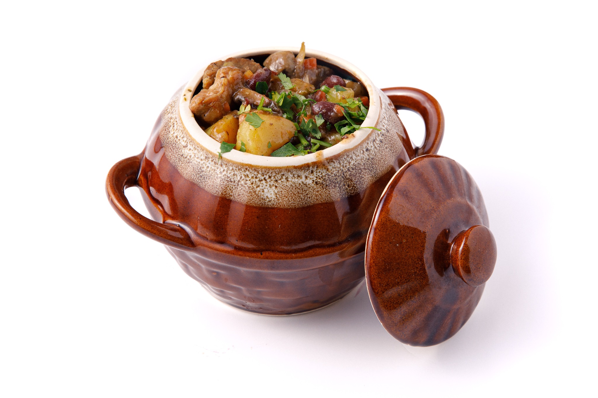Ceramiczny garnek z gulaszem, ziemniakami i ziołami na białym tle, pokrywka obok, usługa cateringowa w Zielonej Górze.