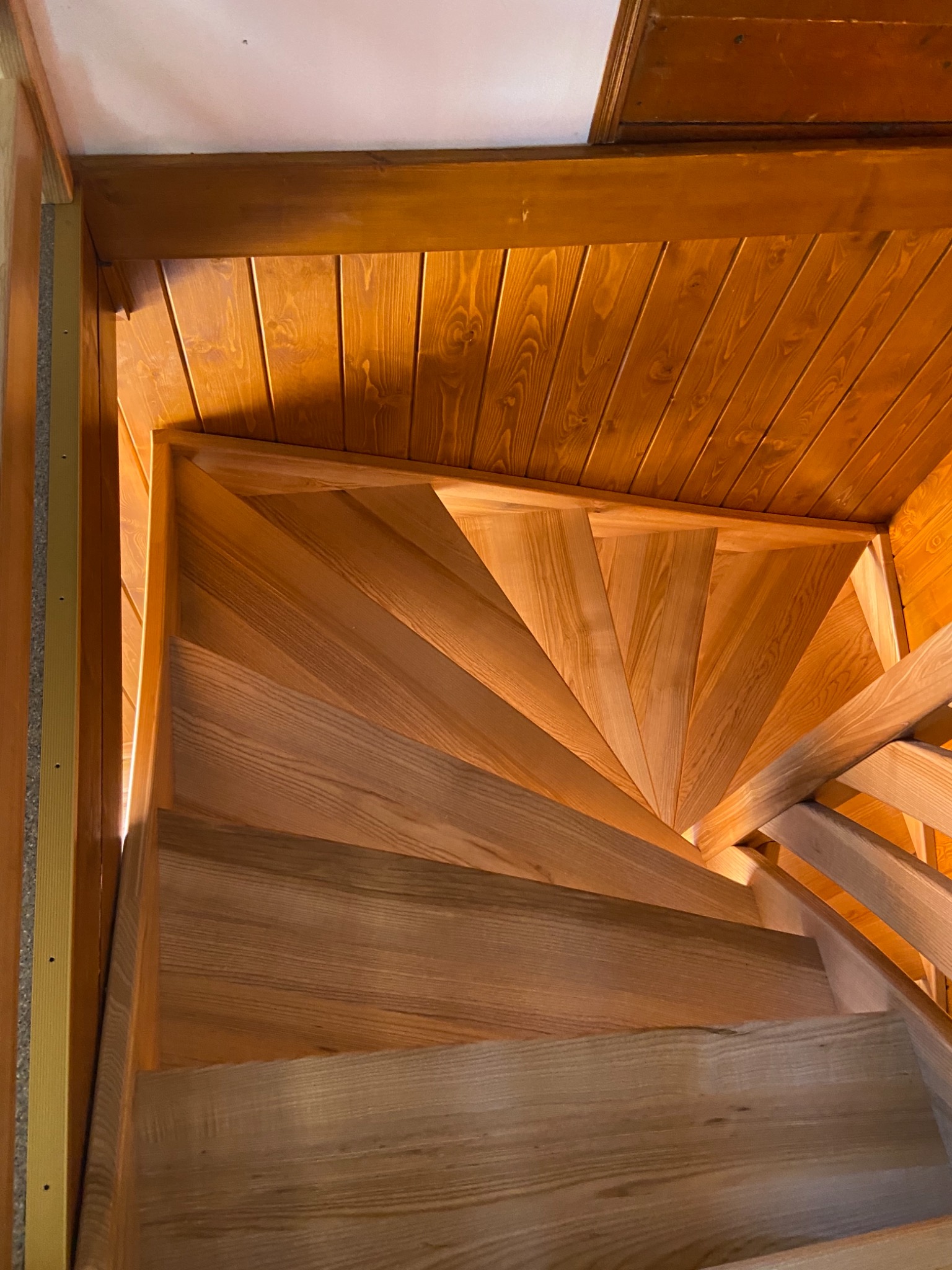 Wewnętrzne, drewniane schody kręcone z jasnego drewna, widok z dołu w górę, drewniana boazeria na ścianach i suficie.