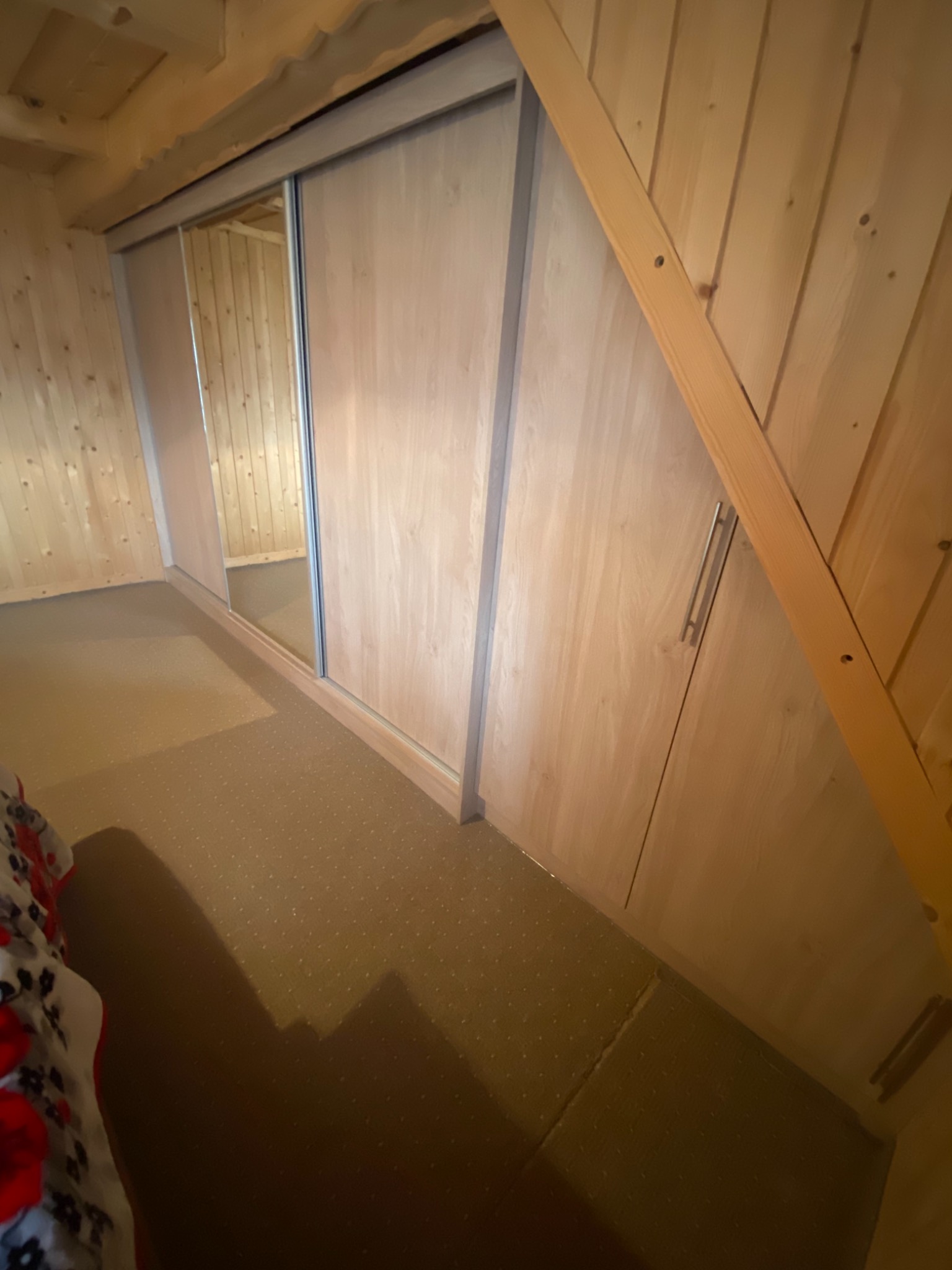 Drewniana zabudowa pod skosem na poddaszu z przesuwnymi drzwiami z lustrzanymi panelami.