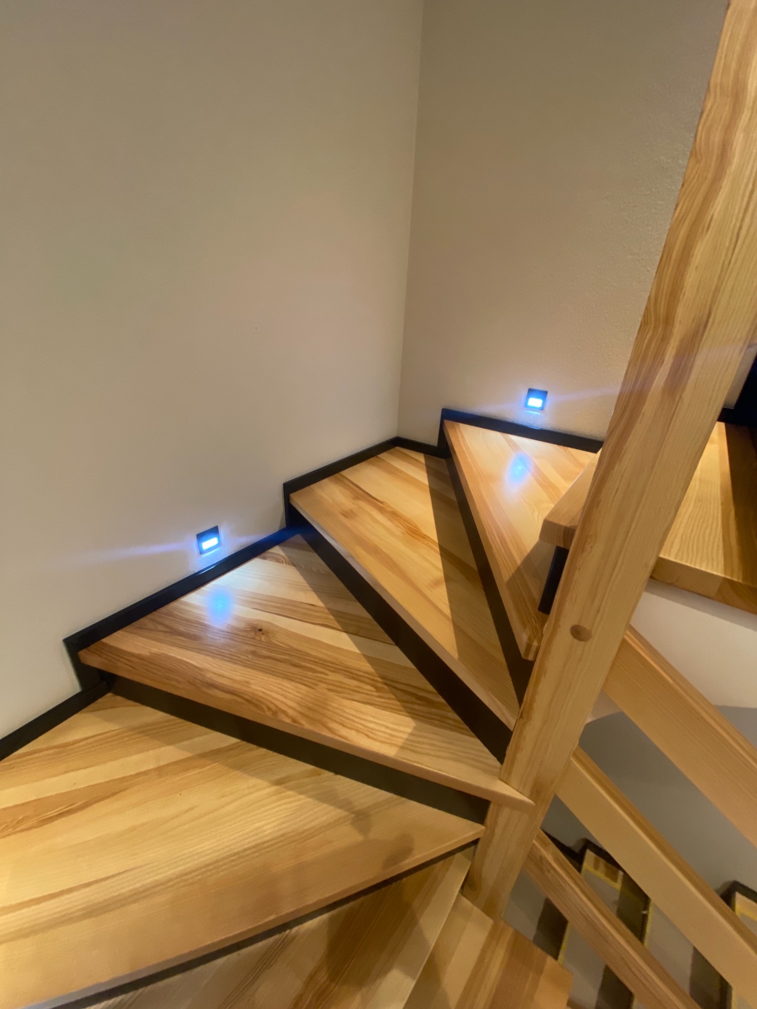 Nowoczesne schody drewniane z podświetleniem LED w ścianie, widok z góry, jasne drewno i czarne obramowanie stopni.
