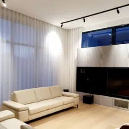 Jasny salon z beżową sofą, białymi, transparentnymi zasłonami i nowoczesną zabudową ściany z telewizorem, oświetlony reflektorami sufitowymi.