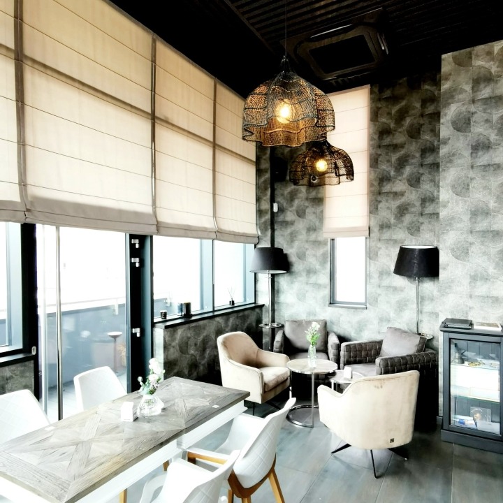Nowoczesne wnętrze z jasnymi roletami rzymskimi, drewnianym stołem i designerskimi lampami wiszącymi w stylu industrialnym.