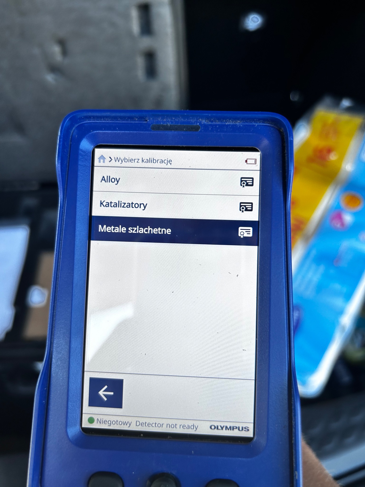 Ekran urządzenia pomiarowego Olympus z menu kalibracji, wyświetlający opcje: Alloy, Katalizatory, Metale szlachetne. Na dole ekranu widoczny status: Niegodowy Detector not ready.