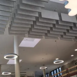 Sufit podwieszany z paneli akustycznych w biurze, oświetlenie LED w kształcie chmur, widoczne elementy konstrukcyjne w tle.