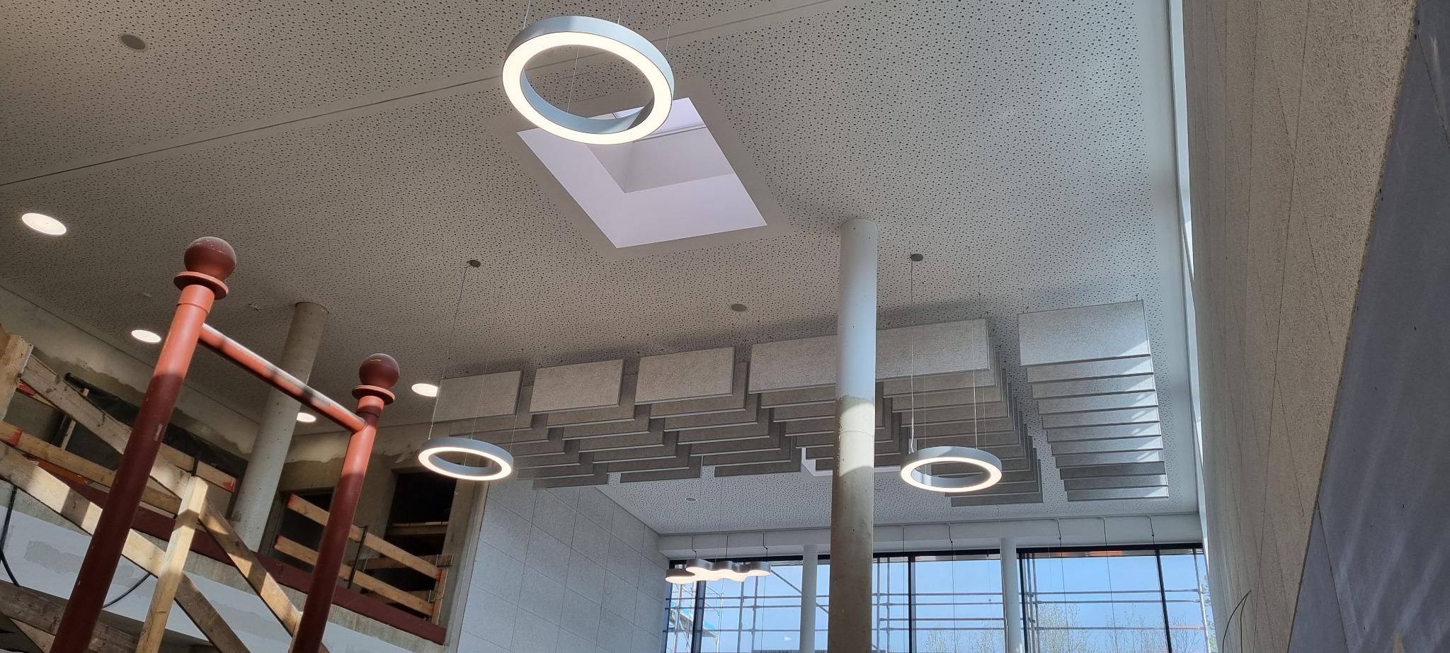 Biuro w trakcie remontu: widoczne sufity podwieszane, nowoczesne okrągłe lampy LED, fragment rusztowania i surowy, betonowy filar.