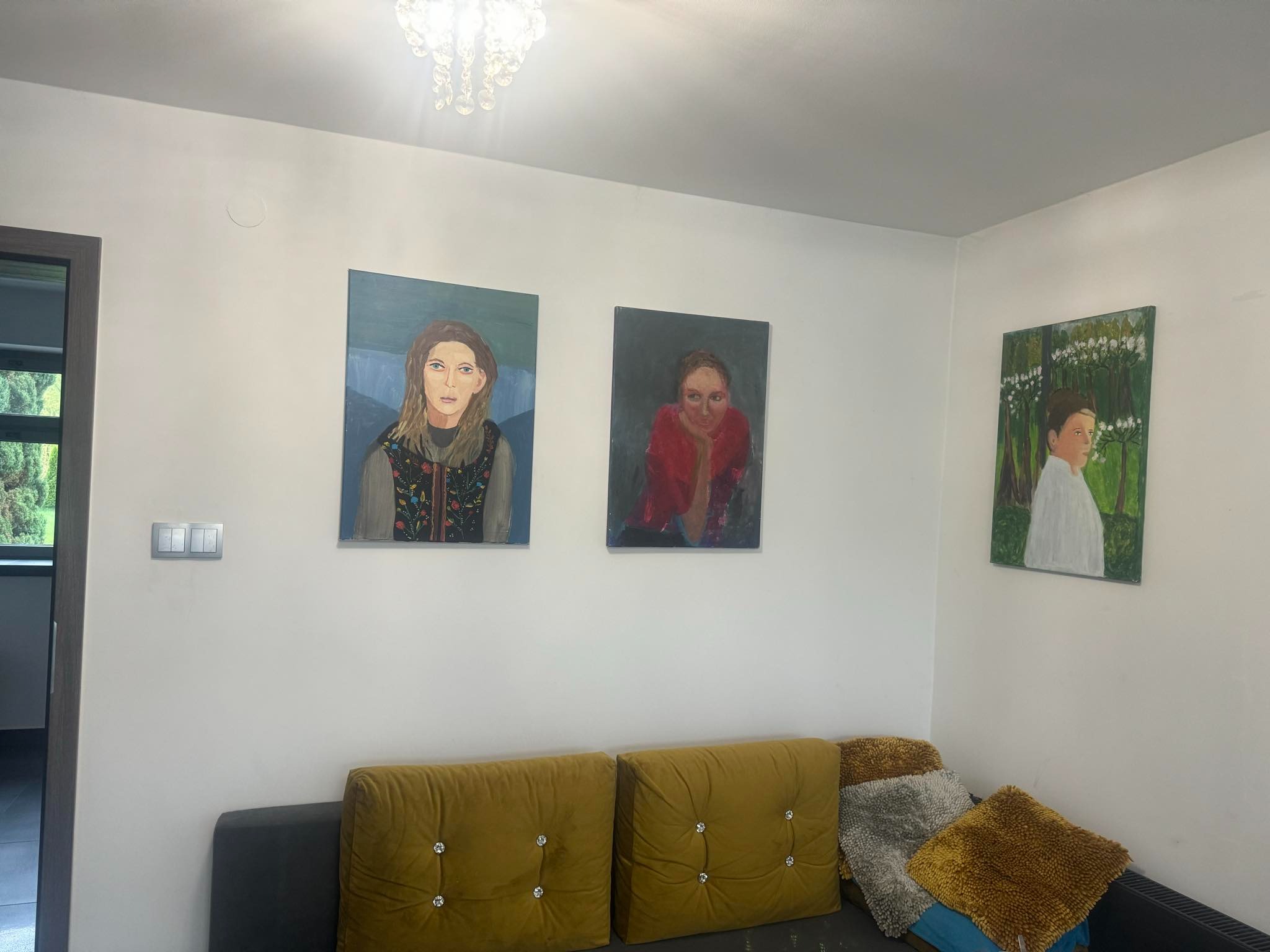 Salon z trzema portretami olejnymi wiszącymi nad sofą z aksamitnymi poduszkami w odcieniach złota i szarości.