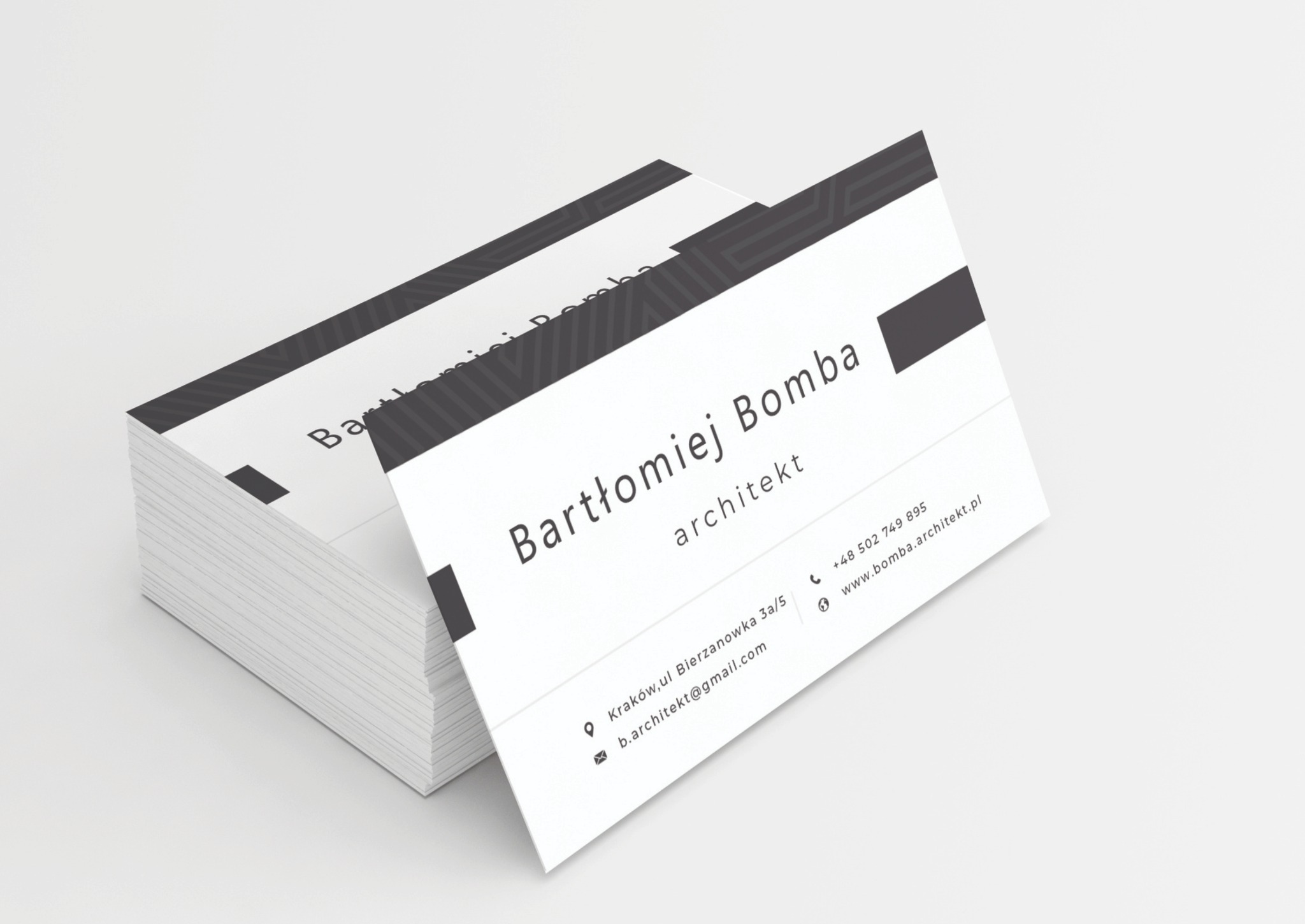 Stos wizytówek architekta Bartłomieja Bomby, minimalistyczny design z czarnymi akcentami na białym tle, widoczne dane kontaktowe i adres.