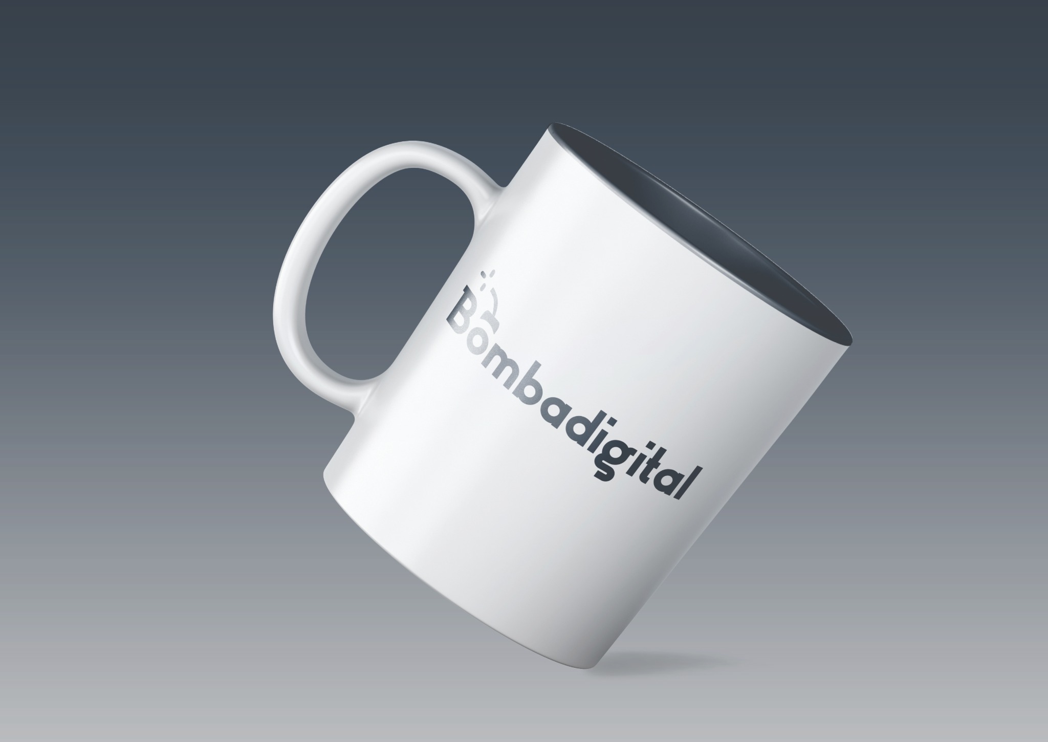 Biały kubek z logo 'Bombadigital' na szarym tle, lekko przechylony, prezentacja identyfikacji wizualnej.
