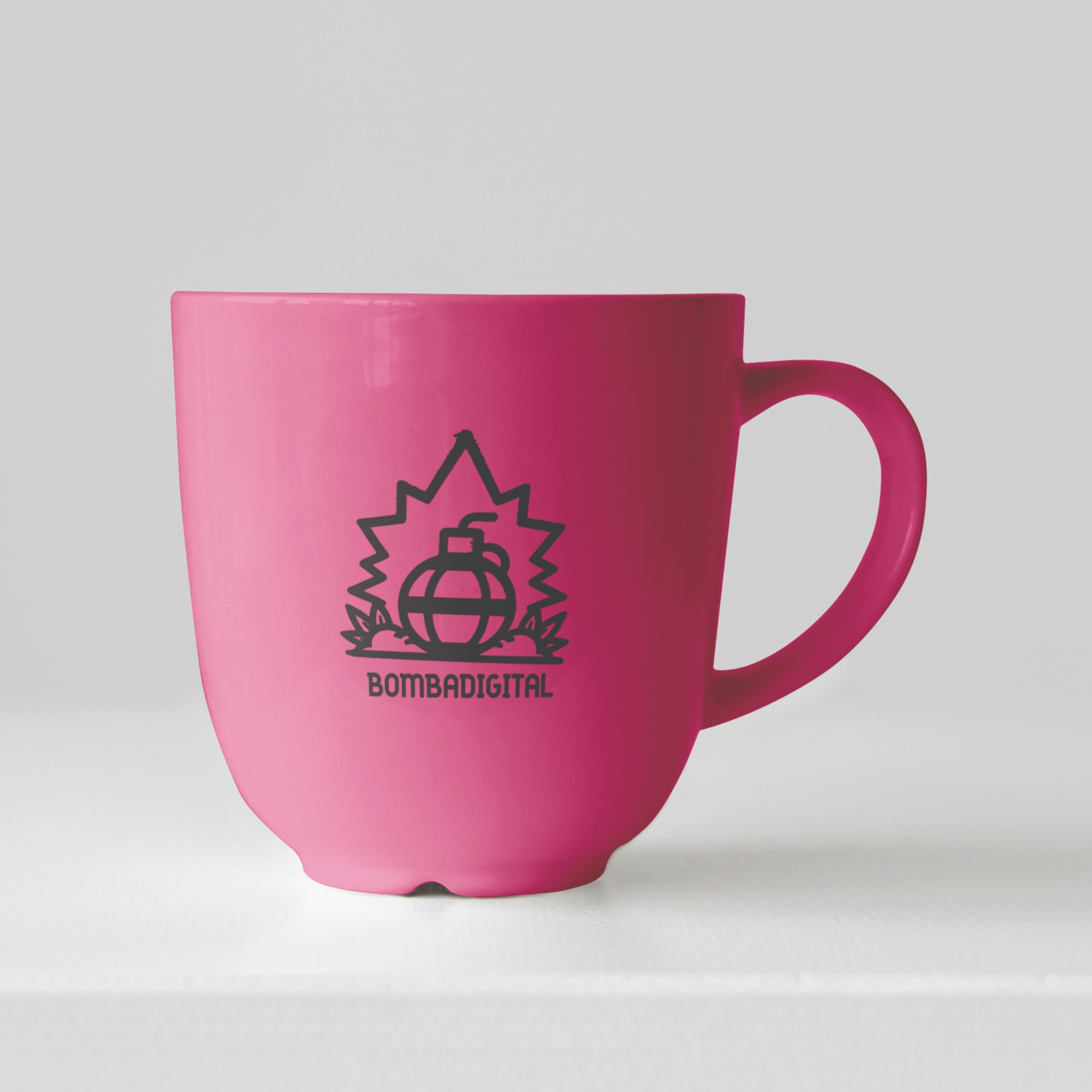 Różowy kubek z czarnym logo przedstawiającym stylizowaną bombę z napisem BOMBADIGITAL na białym tle.