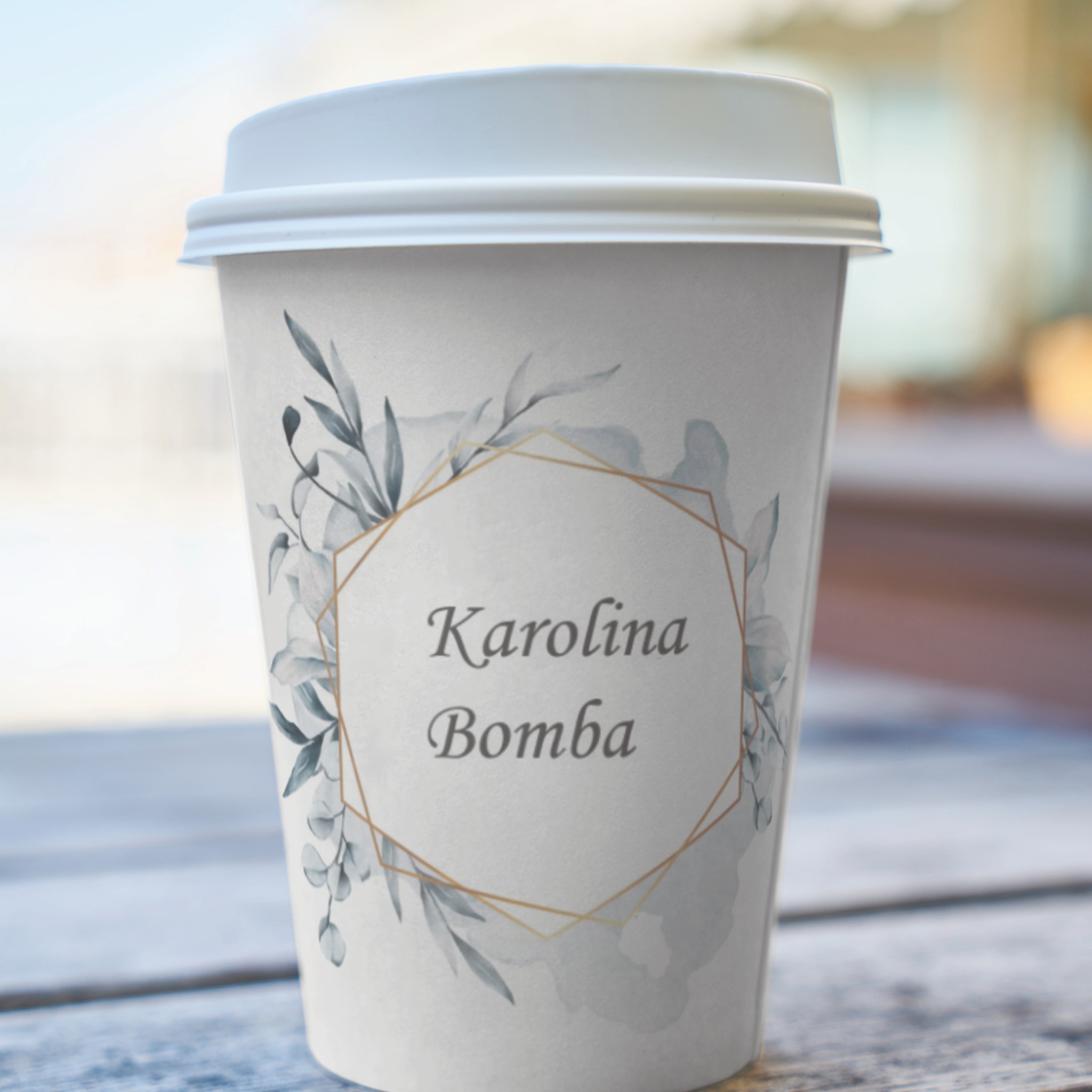 Papierowy kubek z wieczkiem, ozdobiony akwarelowym wzorem liści i złotym geometrycznym ornamentem, zawierający imię i nazwisko 'Karolina Bomba'.