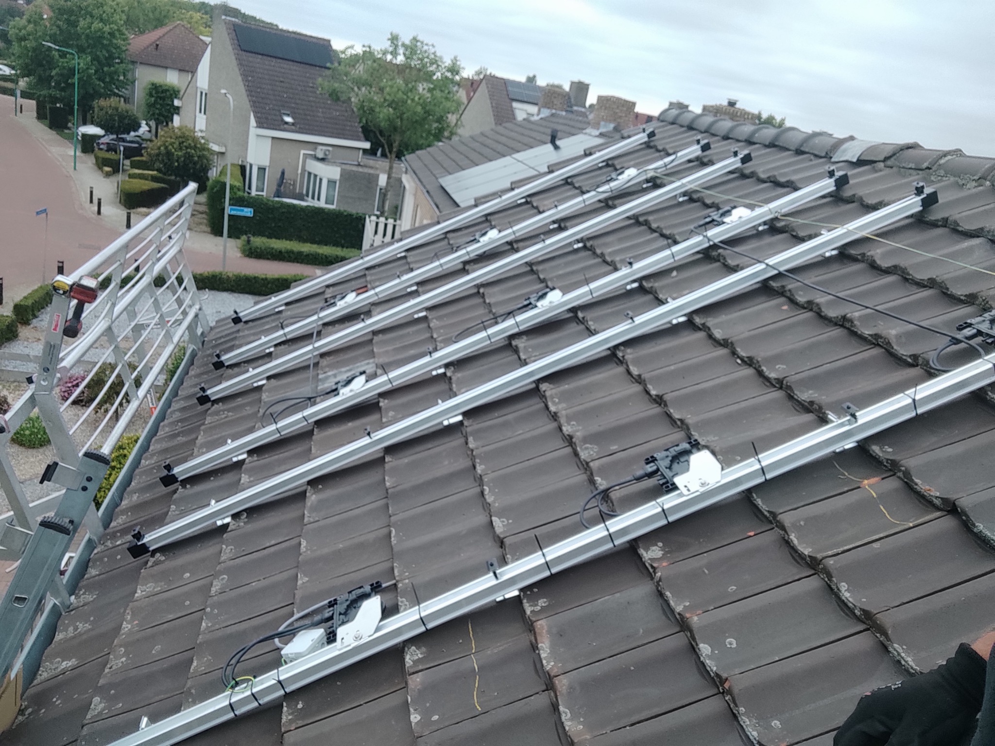 Montaż stelażu pod panele fotowoltaiczne na dachu pokrytym starą dachówką ceramiczną, widoczne aluminiowe profile i elementy mocujące.