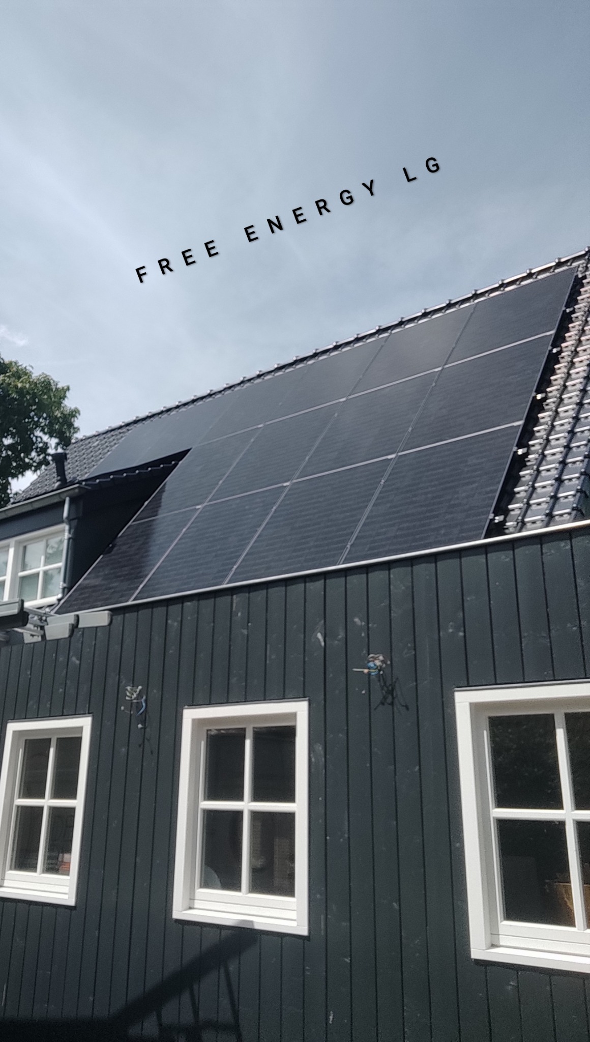 Panele słoneczne na dachu ciemnego, drewnianego domu z białymi oknami, widoczne przewody instalacyjne.