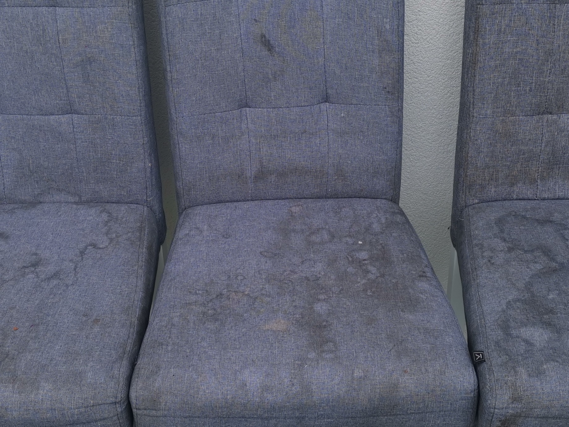 Trzy brudne krzesła tapicerowane z plamami na siedziskach i oparciach, ustawione obok siebie.